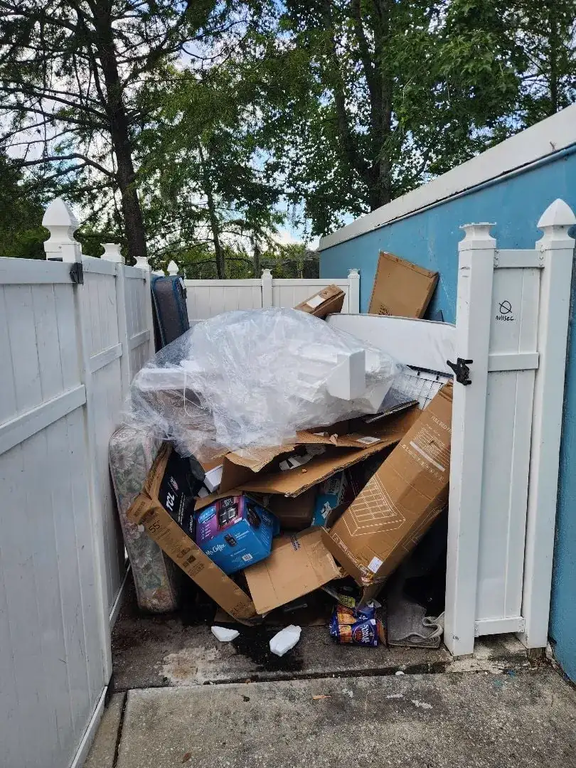 Fenced commercial bulk trash area filled with cardboard and furniture before removal
