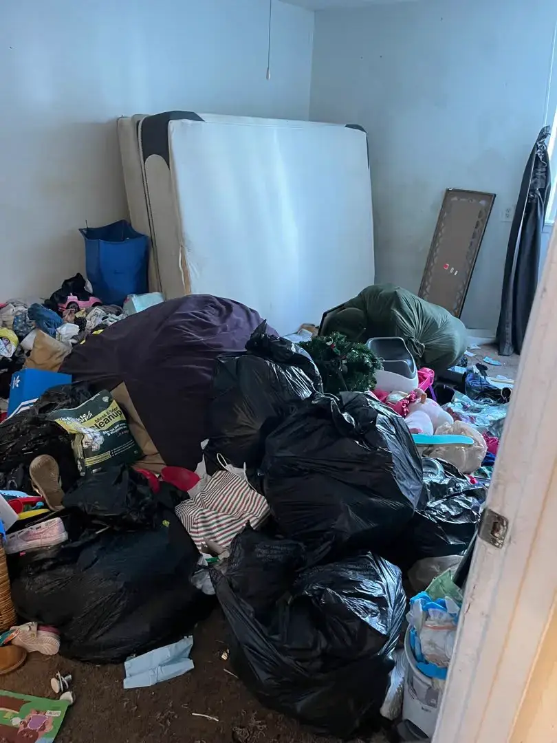 Apartment bedroom filled with furniture and discarded belongings before removal